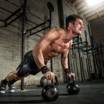 An athlete in shorts and a naked torso does push-ups with weights on the floor